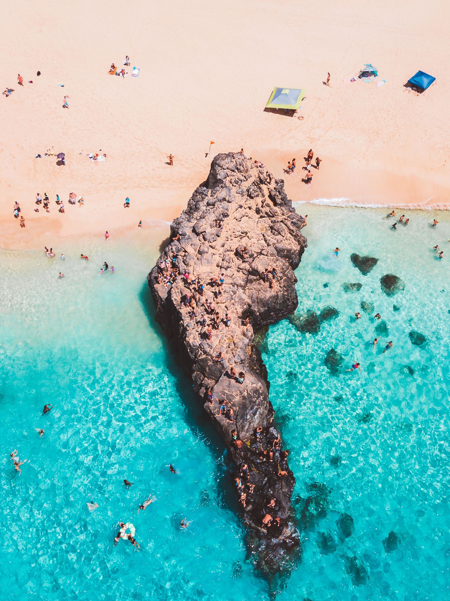Swimmers around a big lava rock in turquoise water