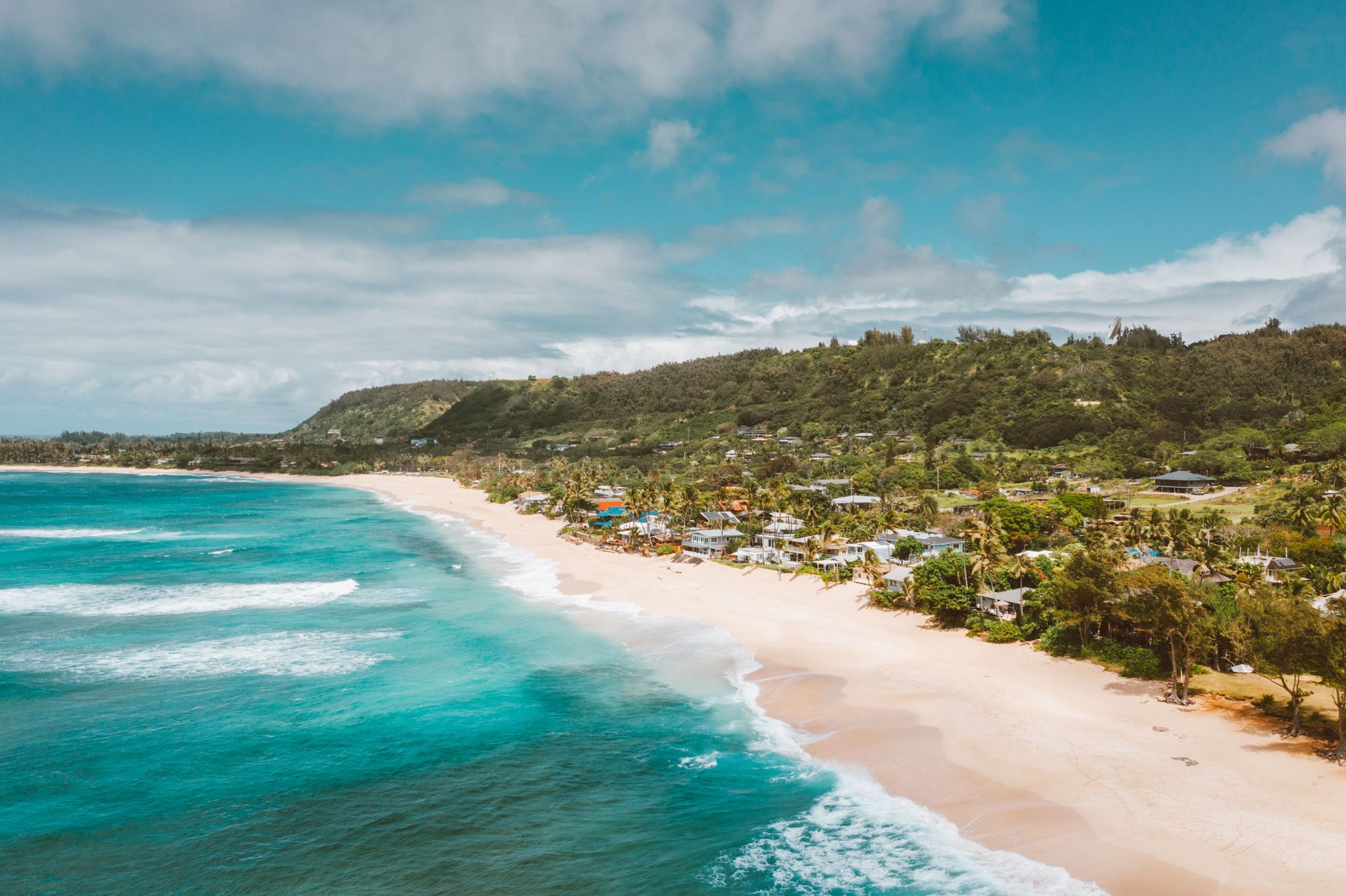 A long golden beach and green hills along the North Shore of Oahu
