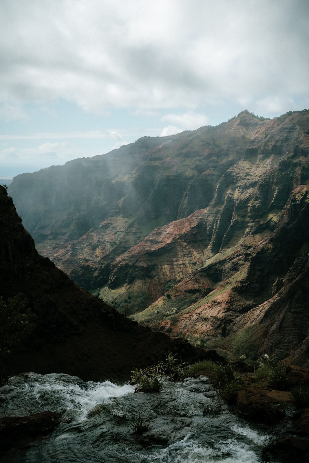 Red and green walls of Waimea Canyon on Kauai, seen from the top of a waterfall